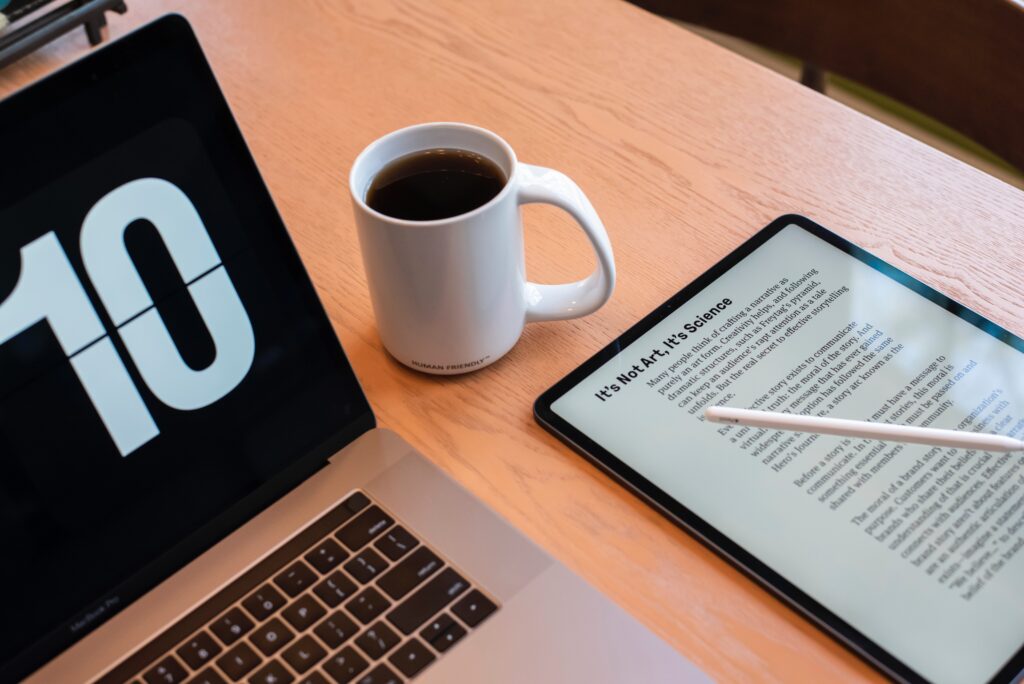 A laptop and tablet open on a table beside a cup of coffee, with an ebook displayed on the tablet.