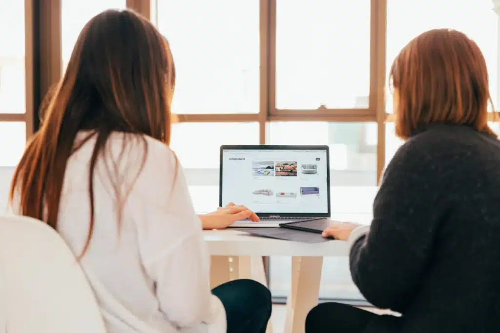 Two female prospects review information on a computer and a tablet as part of a potential customer transaction.