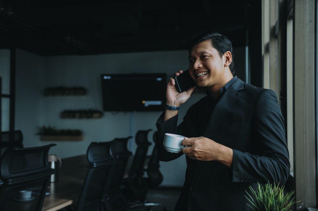 A business executive and person of color chats on a cell phone in an empty conference room on a coffee break to illustrate Account-based marketing tactics.
