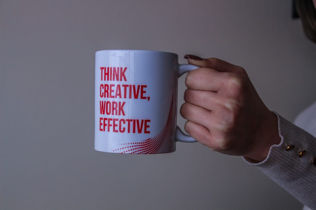 Closeup of a hand grasping a coffee mug; in red capitals the mug reads "Think Creative, Work Effective"