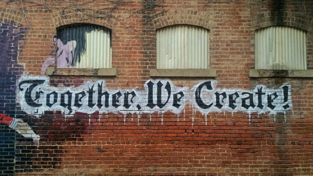 Graffiti on a brick wall reads "Together, we create!" to illustrate the idea.