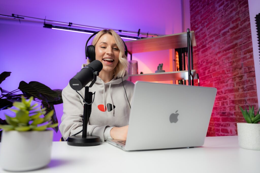 A woman at a laptop speaks into a microphone in a webinar studio.