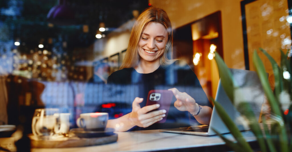Blonde woman sitting at a cafe using smartphone to read email subject lines.