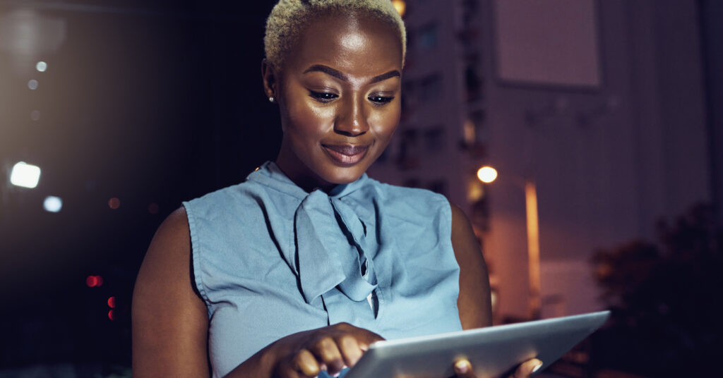 A black woman with short-cropped blonde hair reviews email subject lines on a tablet outside at night.