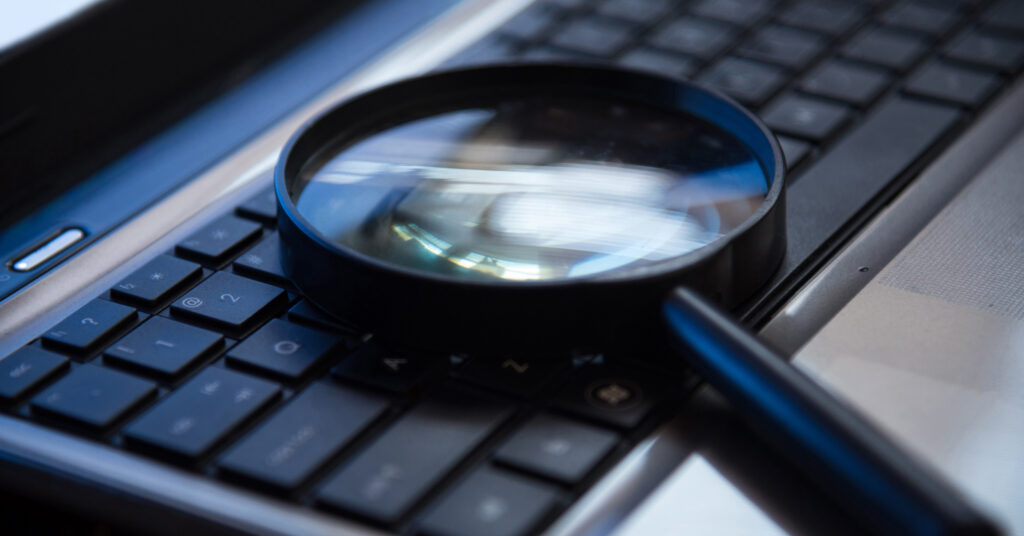A magnifying glass rests on a keyboard to communicate the idea of SEO FAQs