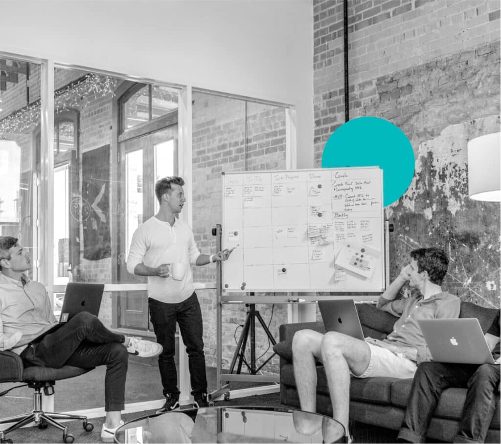 A group of entrepreneurs hammers out email deliverability best practices in an open concept office on a cluttered whiteboard.