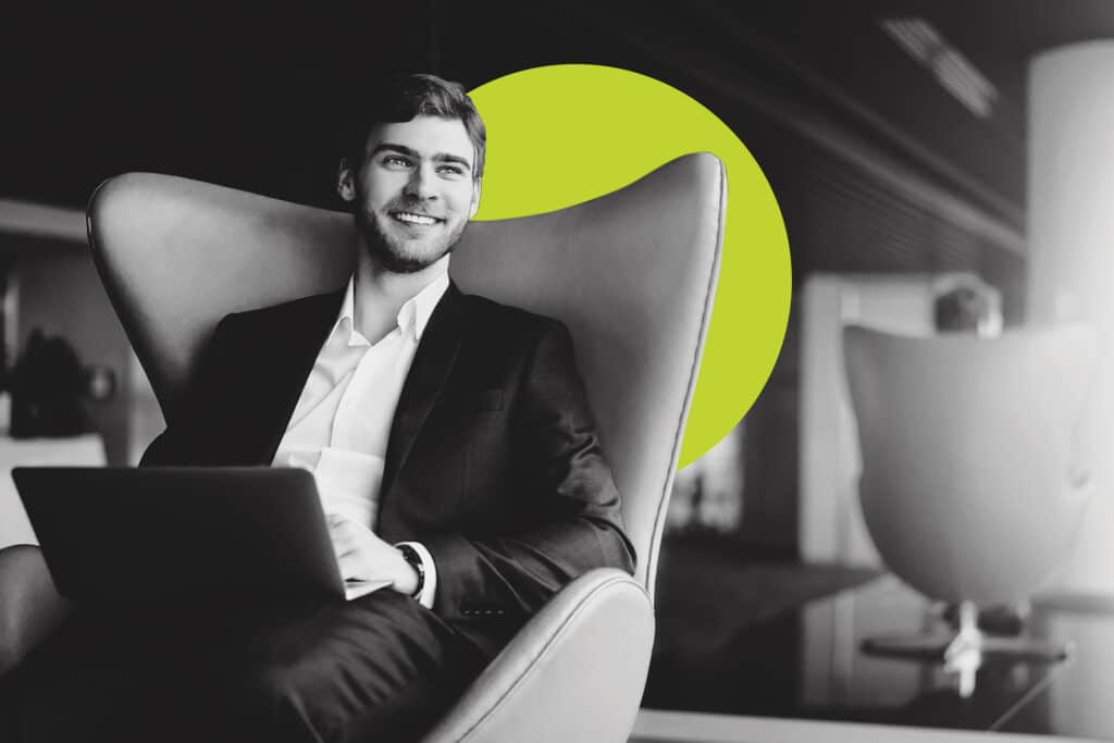 young man sits in an armchair with a laptop smiling with a yellow branded bubble behind him to illustrate digital advertising terms