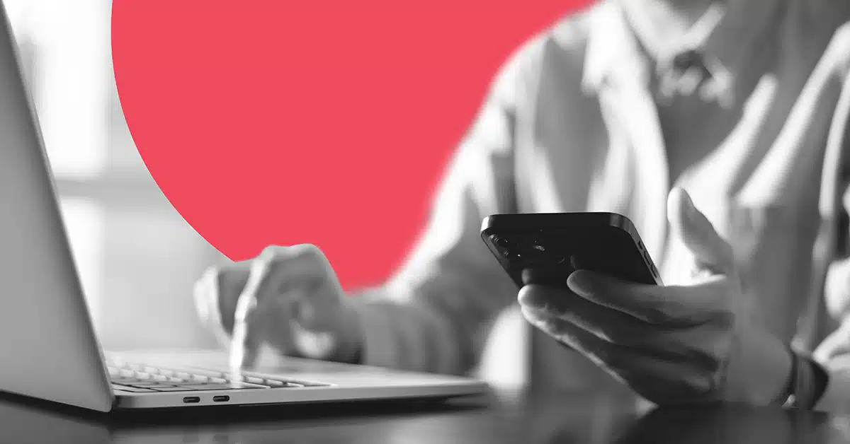 a close up of a user clicking on their laptop while simultaneously using their smart phone