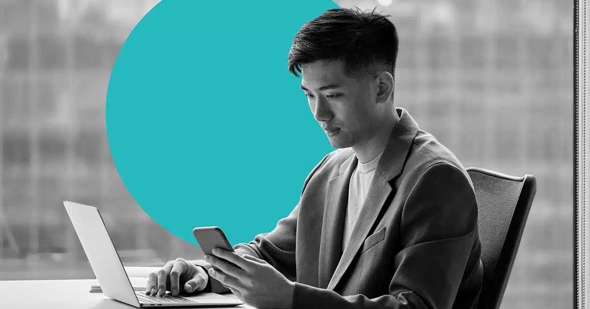 a marketer in a jacket checks a mobile device while working on a laptop