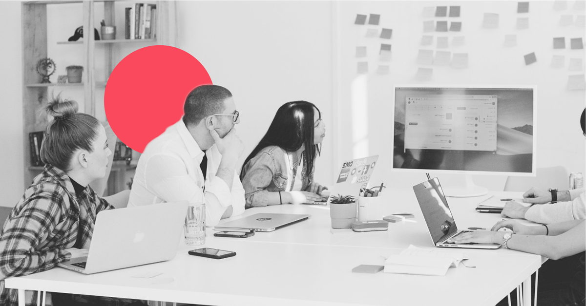 a diverse group of marketers at a conference table study a large shared screen