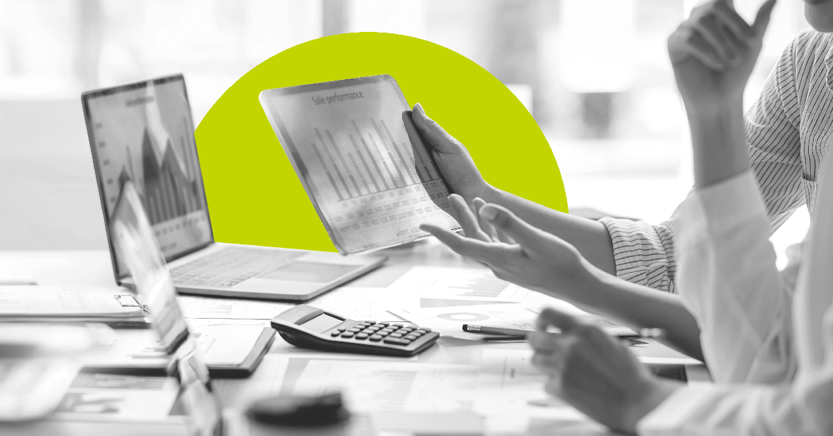 multiple devices, documents and work collected on a conference table with multiple people visibly collaborating