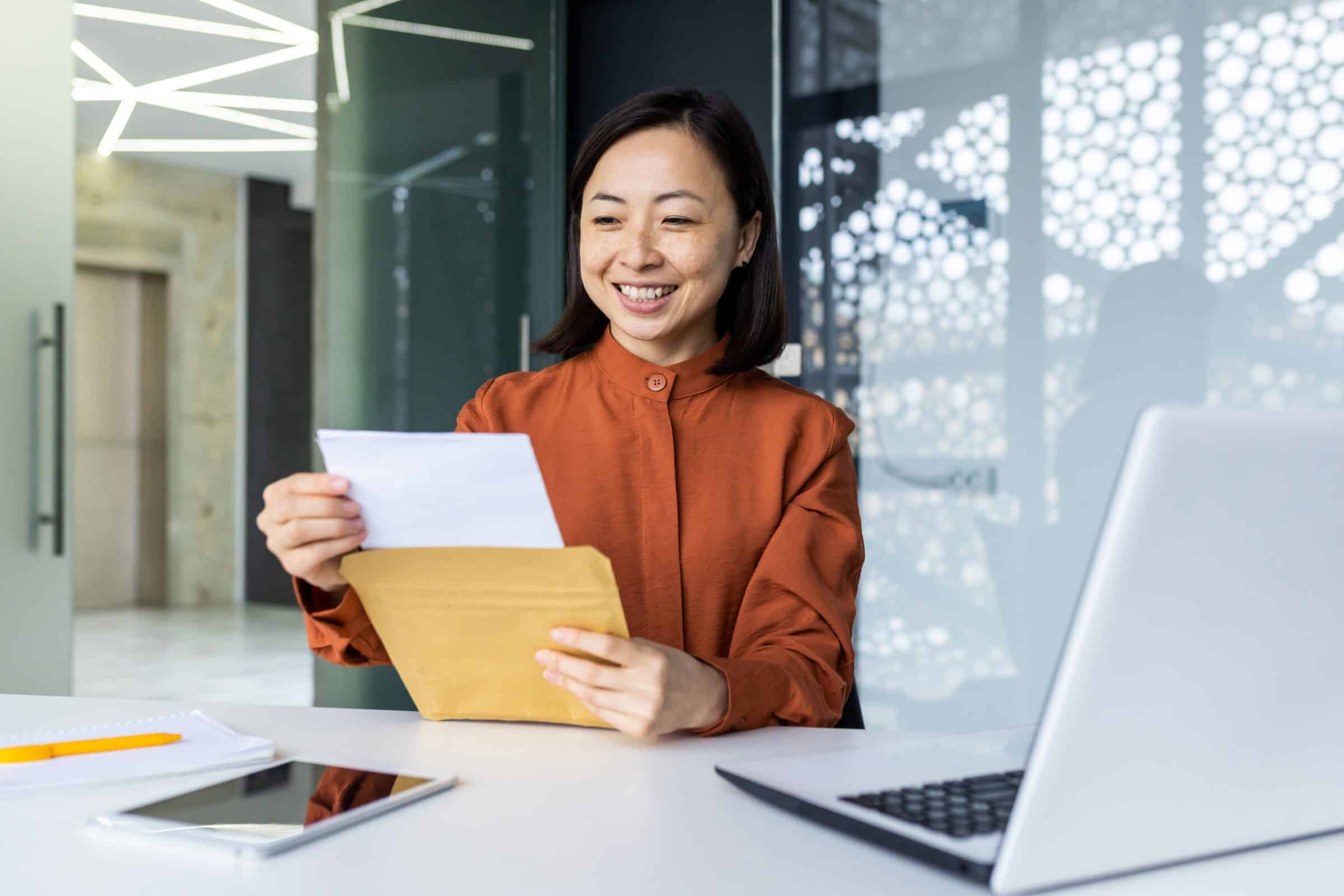 Smiling woman reading a letter at her desk